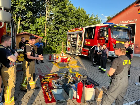 Aktive Feuerwehrdienstleistende vor einem Feuerwehrfahrzeug und Ausrüstung zur technischen Hilfeleistung